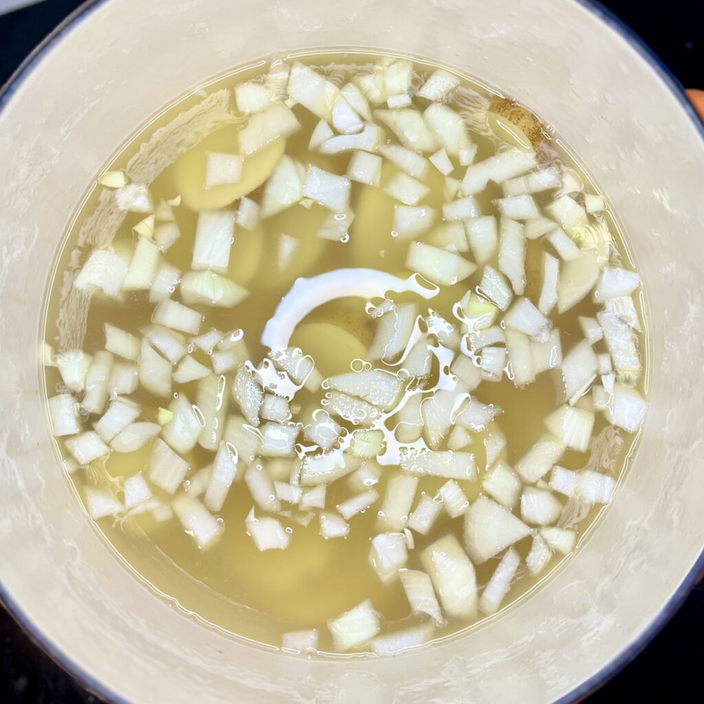 a pot containing broth, water, onion garlic and potatoes 