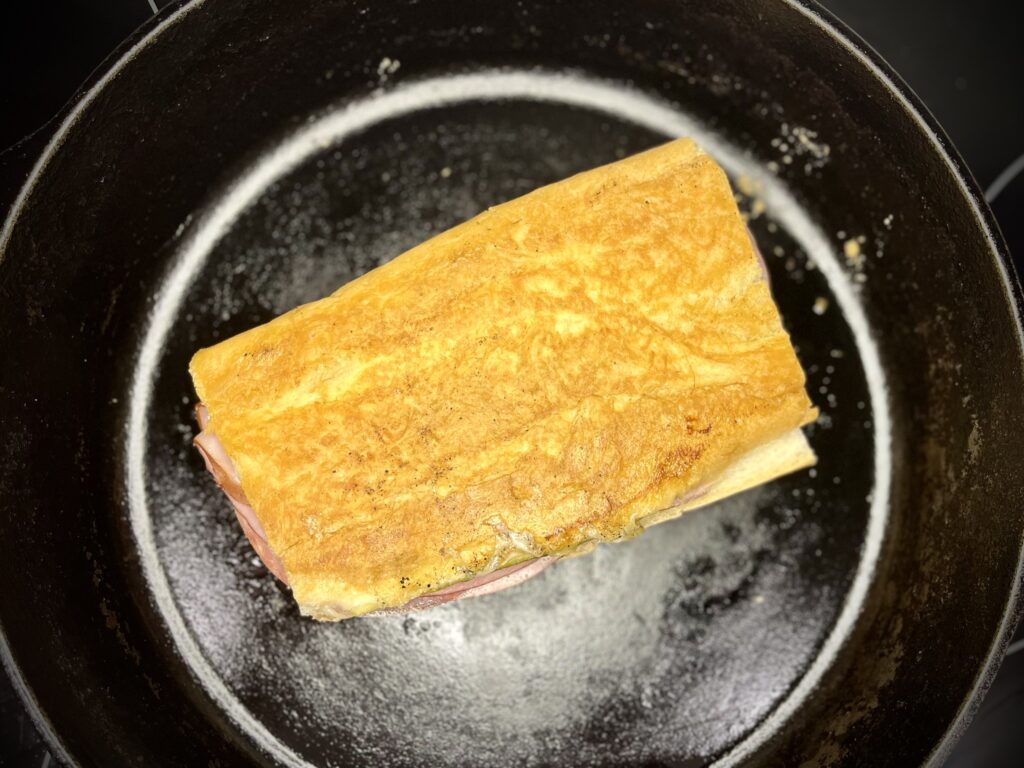 a sandwich being pressed in a cast iron skillet