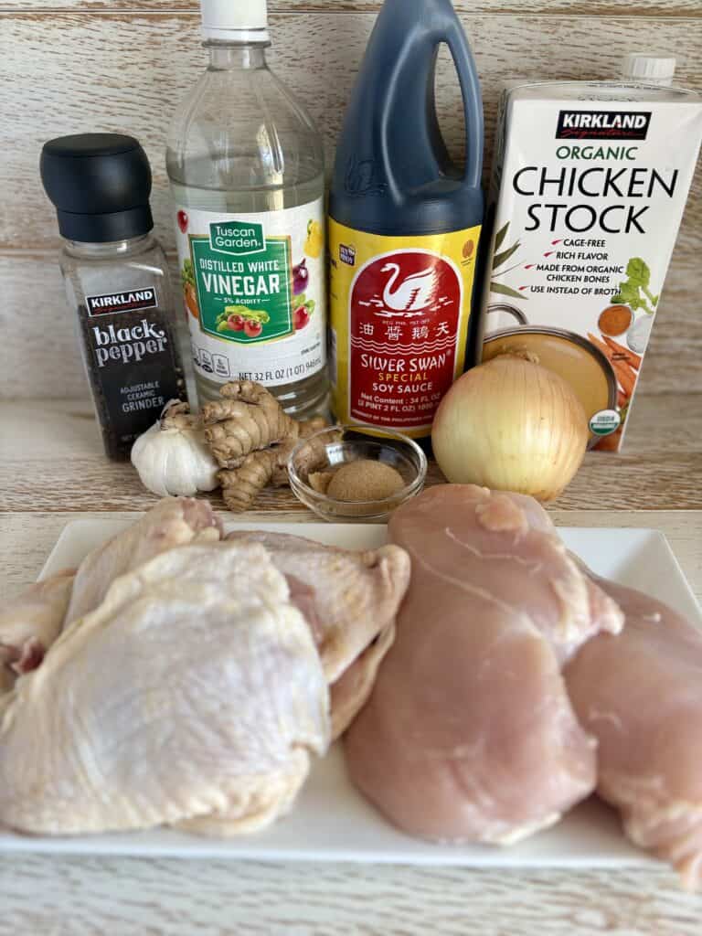 Raw chicken thighs and breasts with garlic, ginger, soy sauce, vinegar, chicken stock, and seasonings on a wooden kitchen countertop.