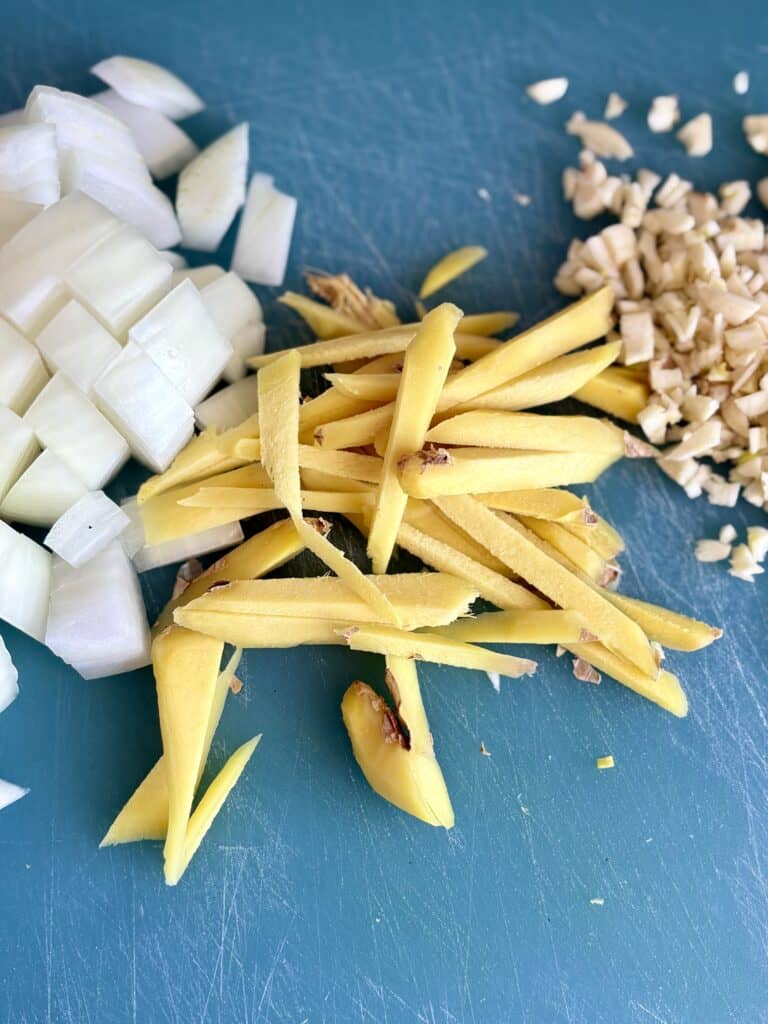 Fresh chopped onions, garlic, and ginger on a blue cutting board, ready for cooking or recipe preparation.