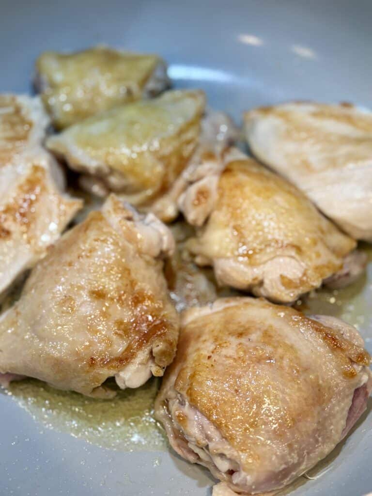 Golden chicken thighs sizzling in a skillet with a crispy, browned exterior.