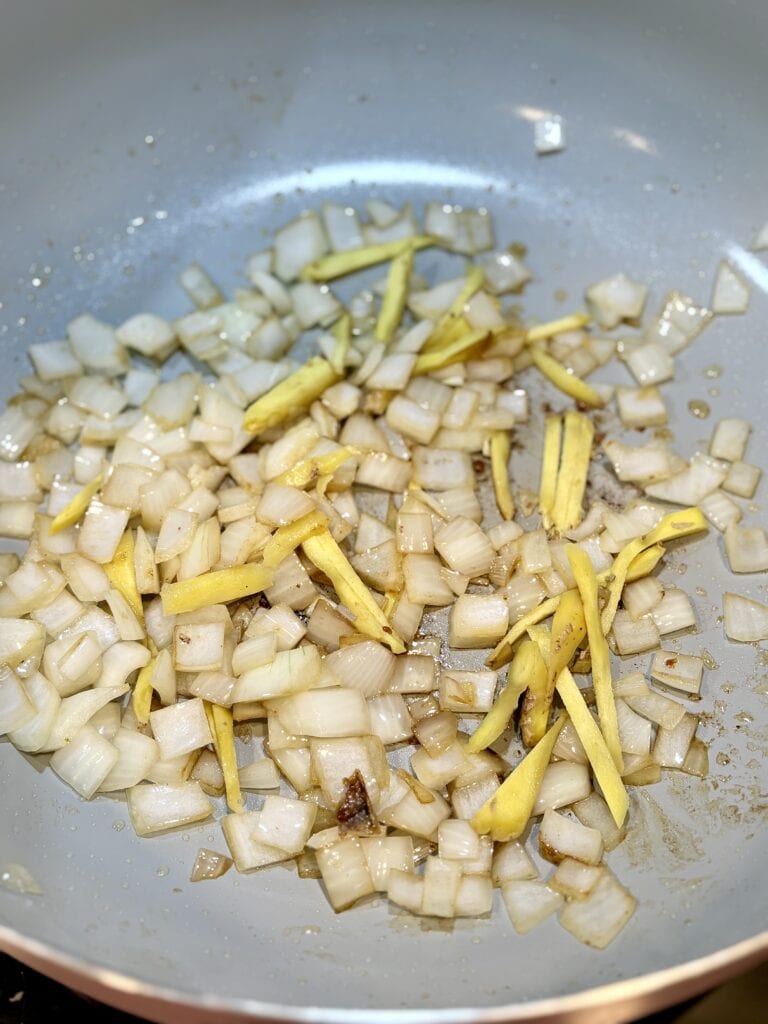 Sautéing chopped onions and fresh ginger in a non-stick skillet for a flavorful base in cooking adobo. Perfect for preparing delicious homemade dishes with aromatic ingredients.