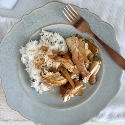 Delicious homemade filipino chicken adobo and rice served on a light blue plate with a copper fork, perfect for a comforting meal.