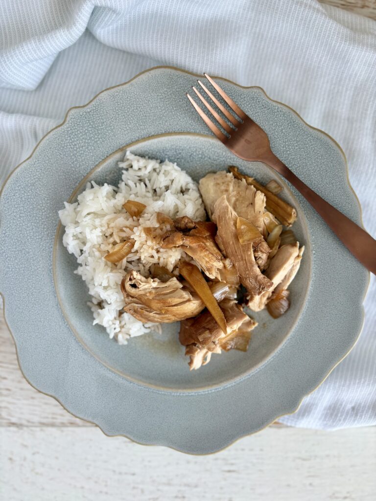 Delicious homemade filipino chicken adobo and rice served on a light blue plate with a copper fork, perfect for a comforting meal.