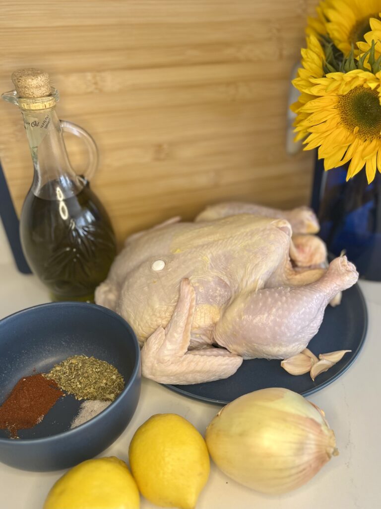 An uncooked chicken with lemons, seasoning, onion and oil on a plate on the counter