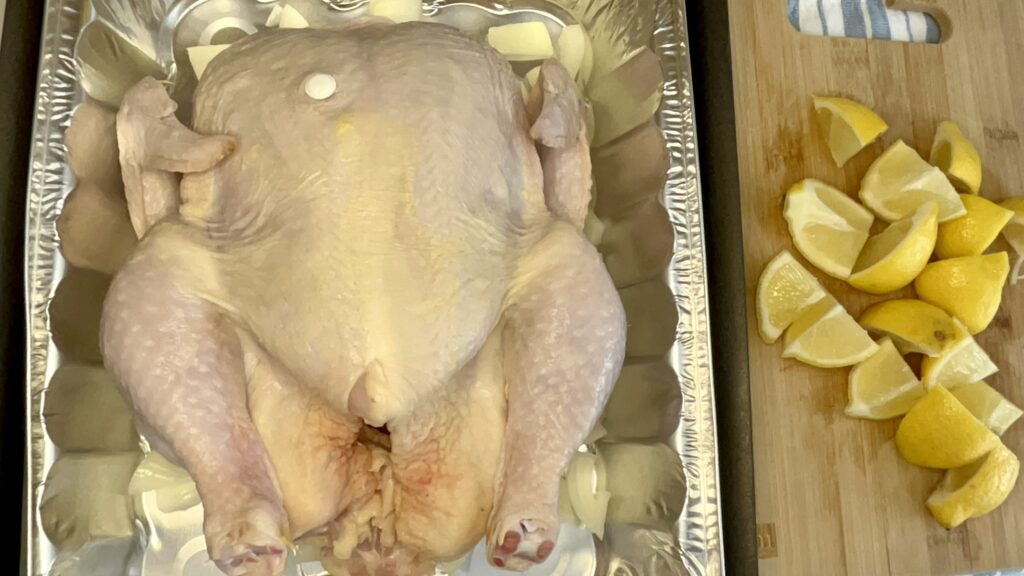 Uncooked chicken in a roasting pan with quartered lemon pieces.
