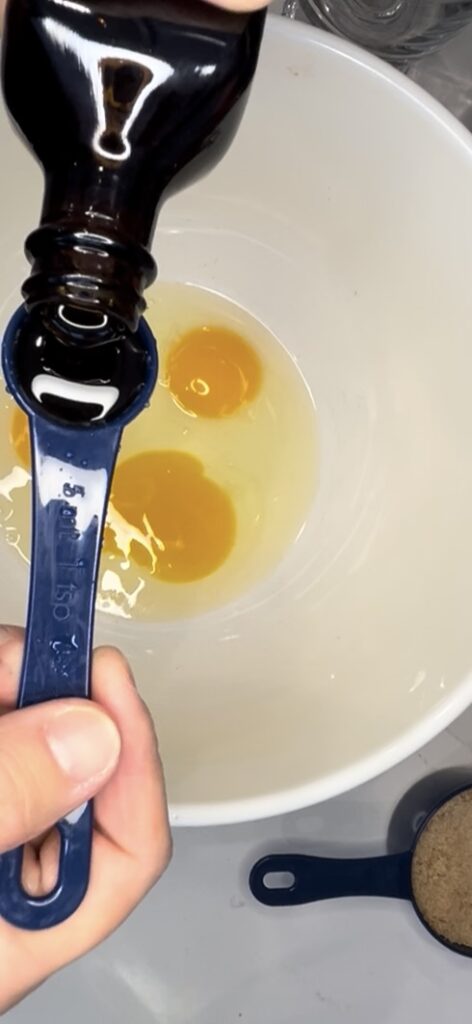 pouring vanilla extract in a measuring spoon and eggs in a bowl