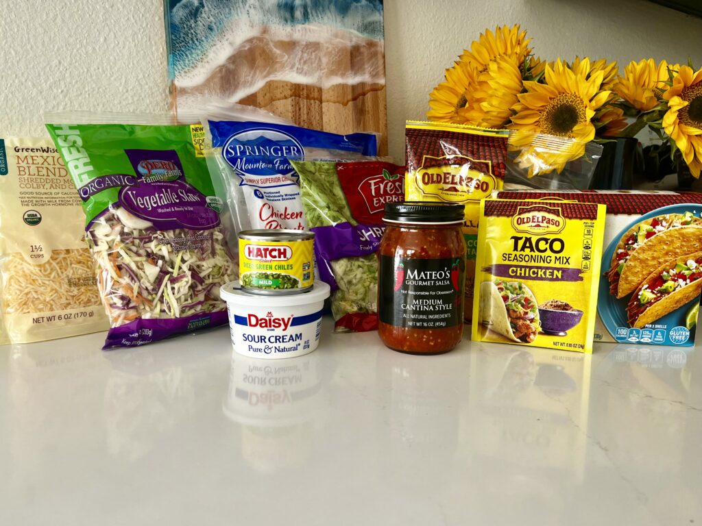 Ingredients- Mexican blend cheese, shredded cabbage, shredded lettuce, sour cream, diced green chiles, salsa, chicken taco seasoning mix, hard taco shells, soft tacos on the counter 