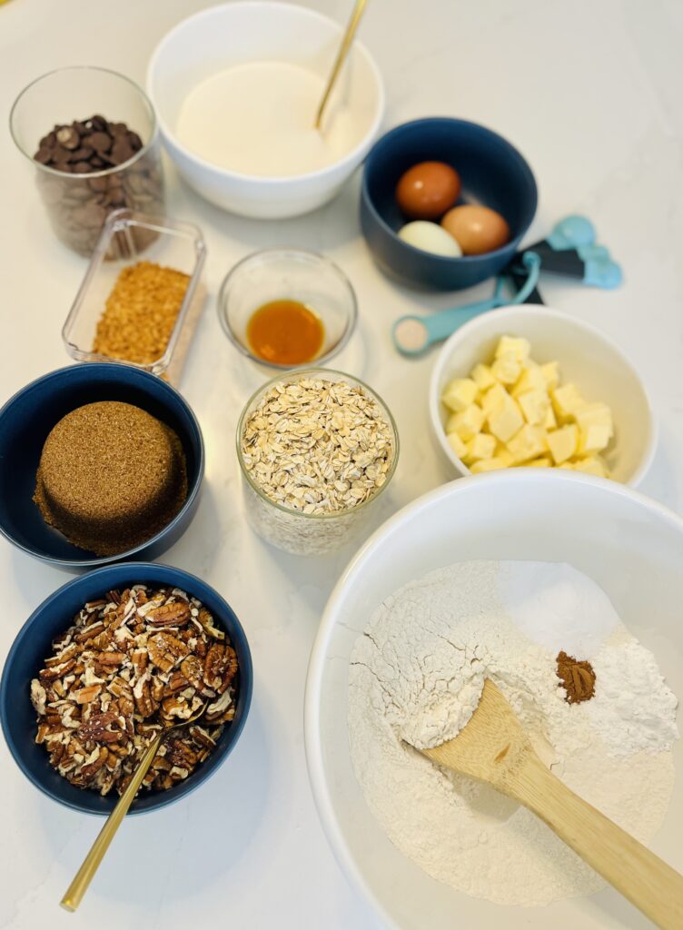  butter, baking powder, baking soda, salt, flour, cinnamon, granulated sugar, dark brown sugar, eggs, vanilla extract, semi-sweet chocolate chips, dark chocolate chips, old-fashioned rolled oats, toasted coconut flakes. chopped pecans on the counter 
