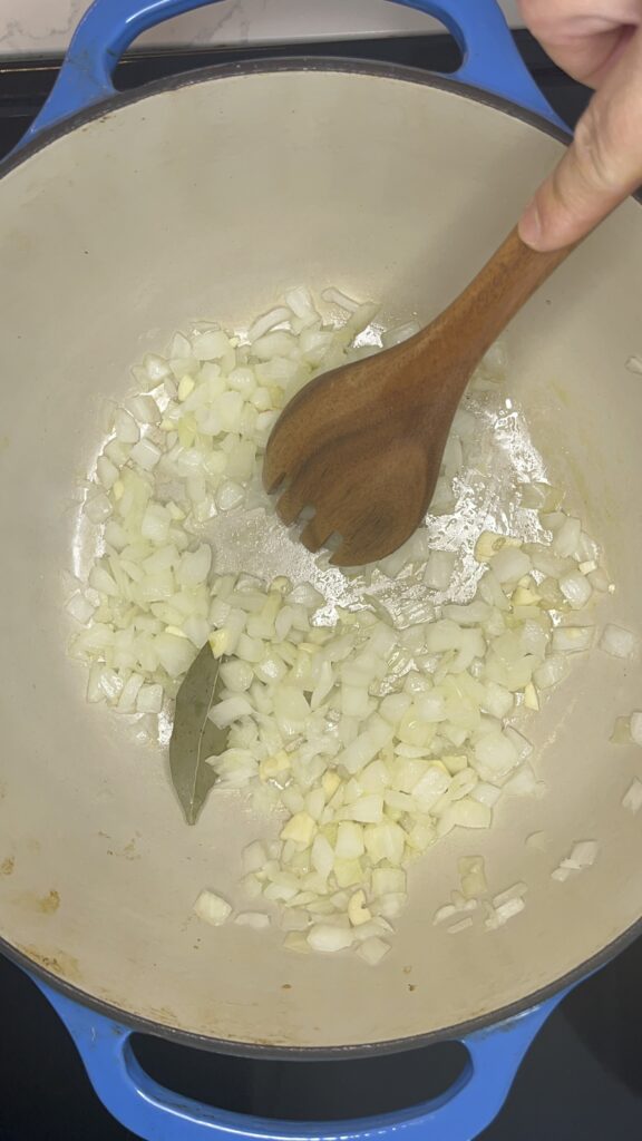 Stirring onion and garlic and bay leaf in stockpot.
