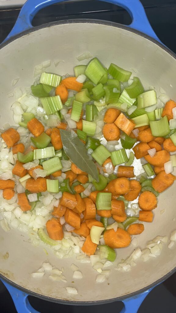 carrots, celery, onions, garlic, bay leaf in stockpot cooking.
