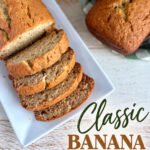 Freshly sliced classic banana bread on a white plate with a whole loaf in the background, perfect for breakfast or snack.