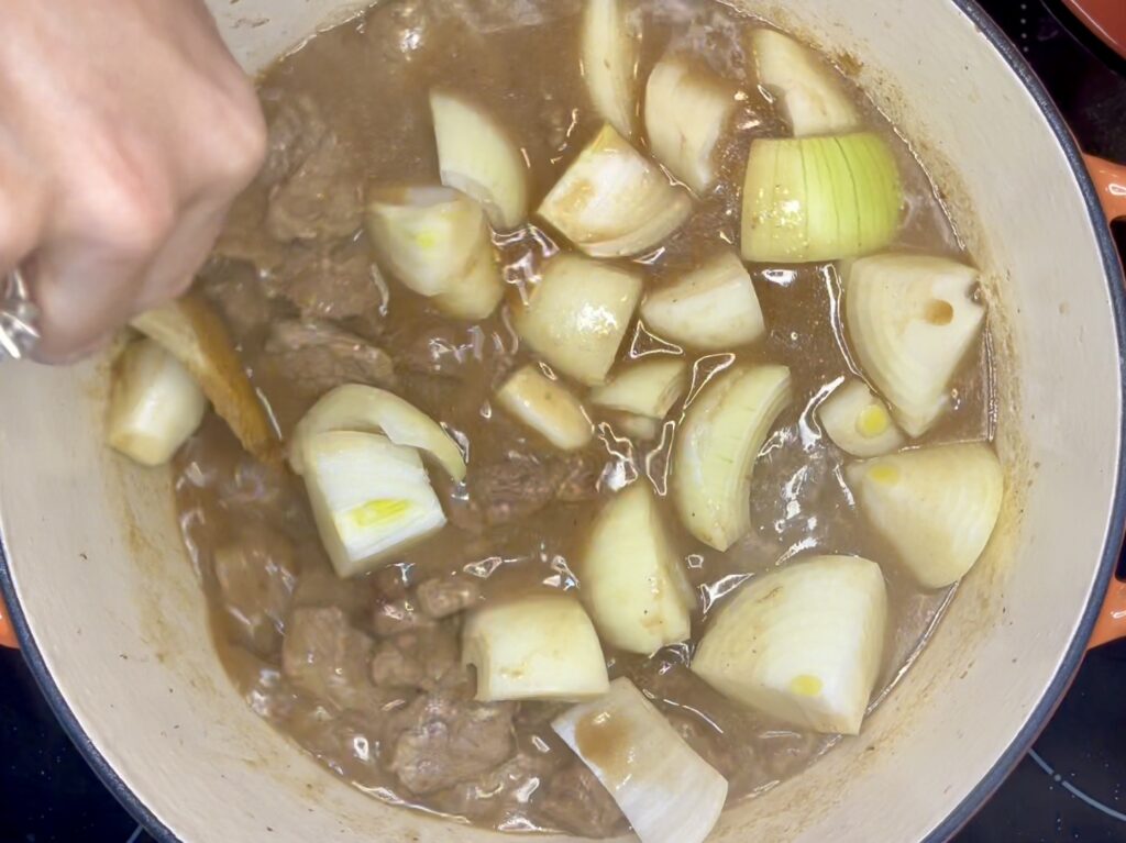 onions being stirred into pot with beef and broth