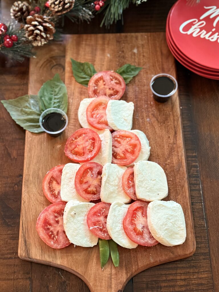 Caprese Salad ingredients in the shape of a Christmas Tree on a brown cutting board on the dining room table.