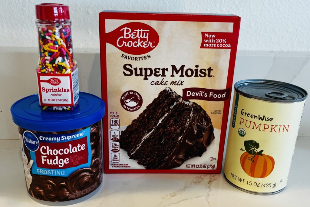 Devil's food cake mix, 15 oz can of pumpkin puree, chocolate fudge frosting, and rainbow sprinkles on the counter