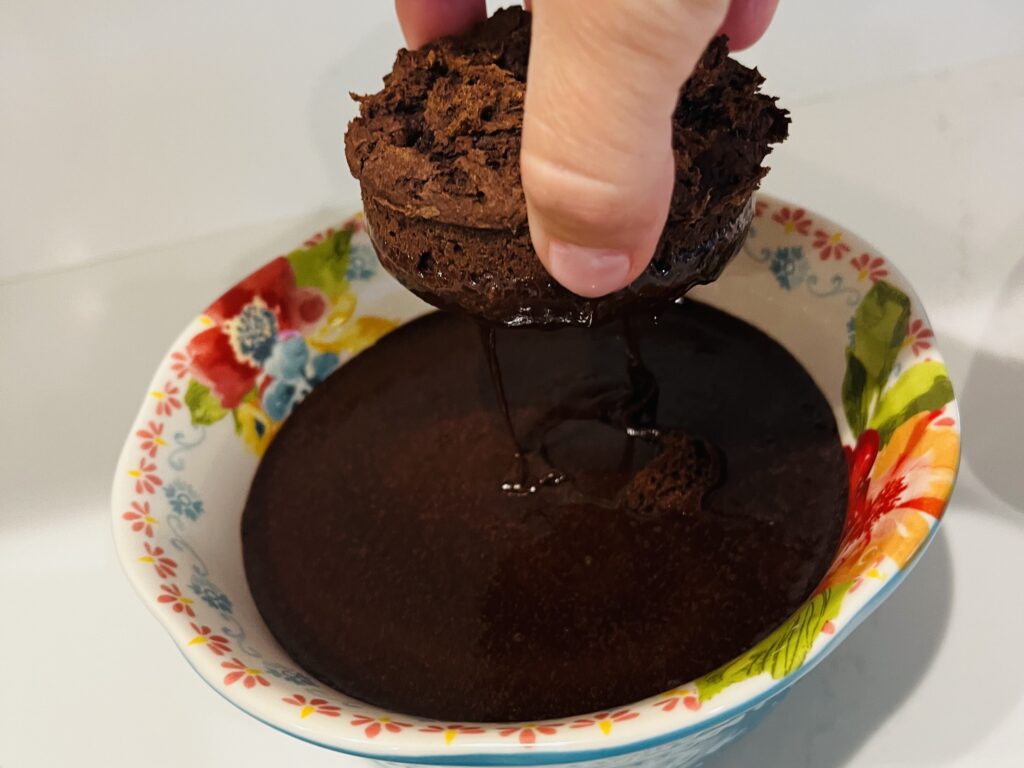 Dipping caked donuts into chocolate fudge icing in a bowl