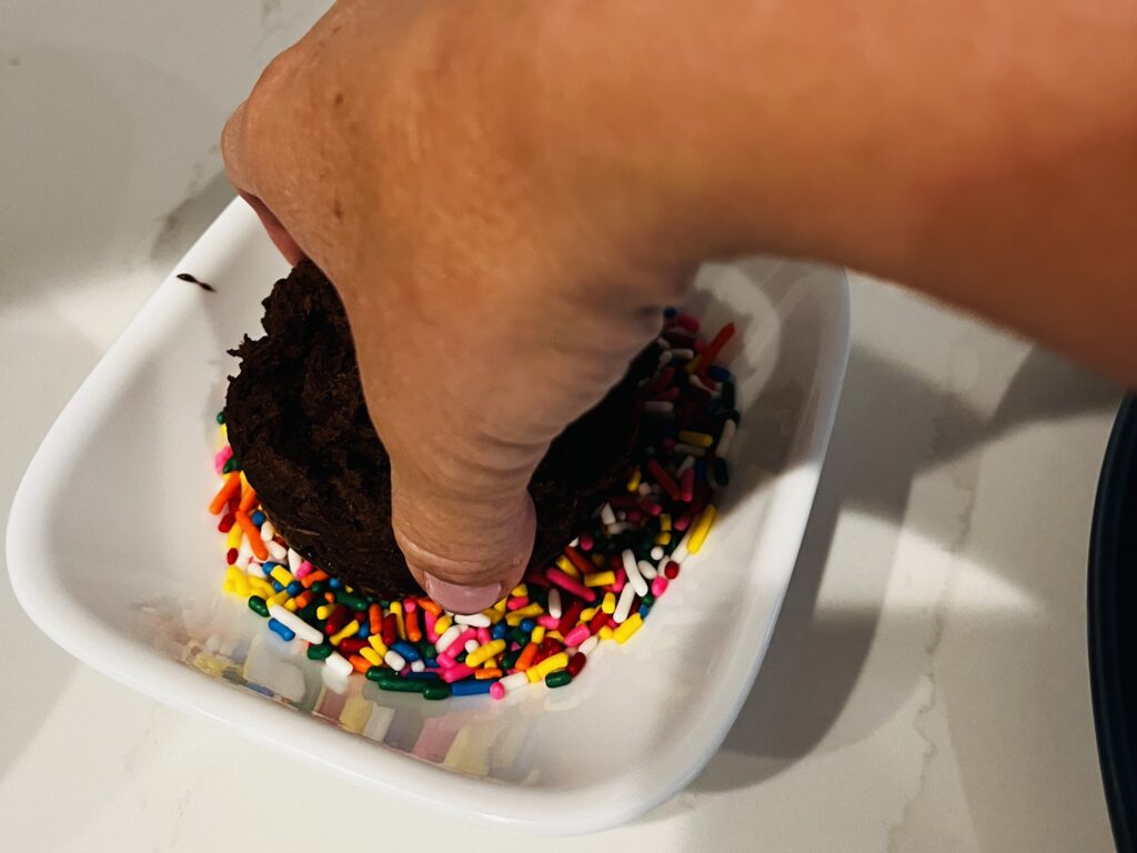 Dipping iced donuts into a small bowl with sprinkles