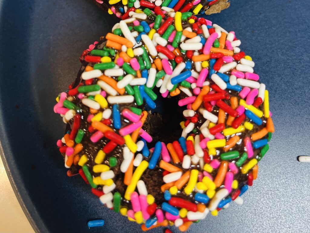 Chocolate donut with chocolate fudge icing with sprinkles on top.