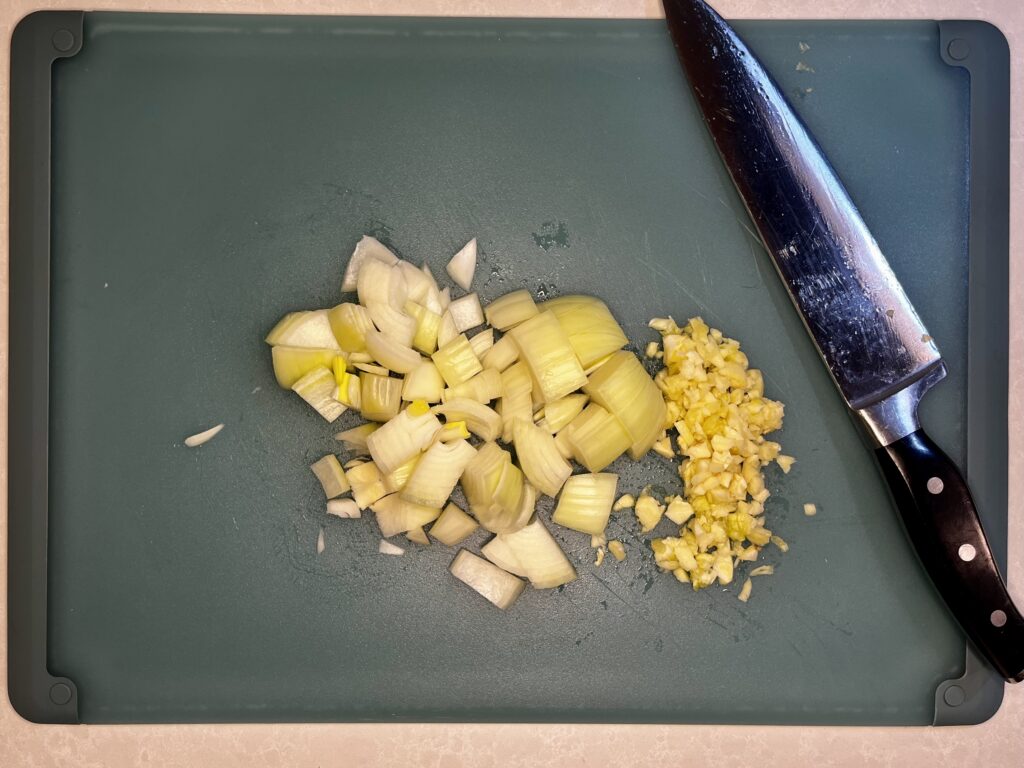 minced garlic and diced onion on a cutting board with a chef's knife