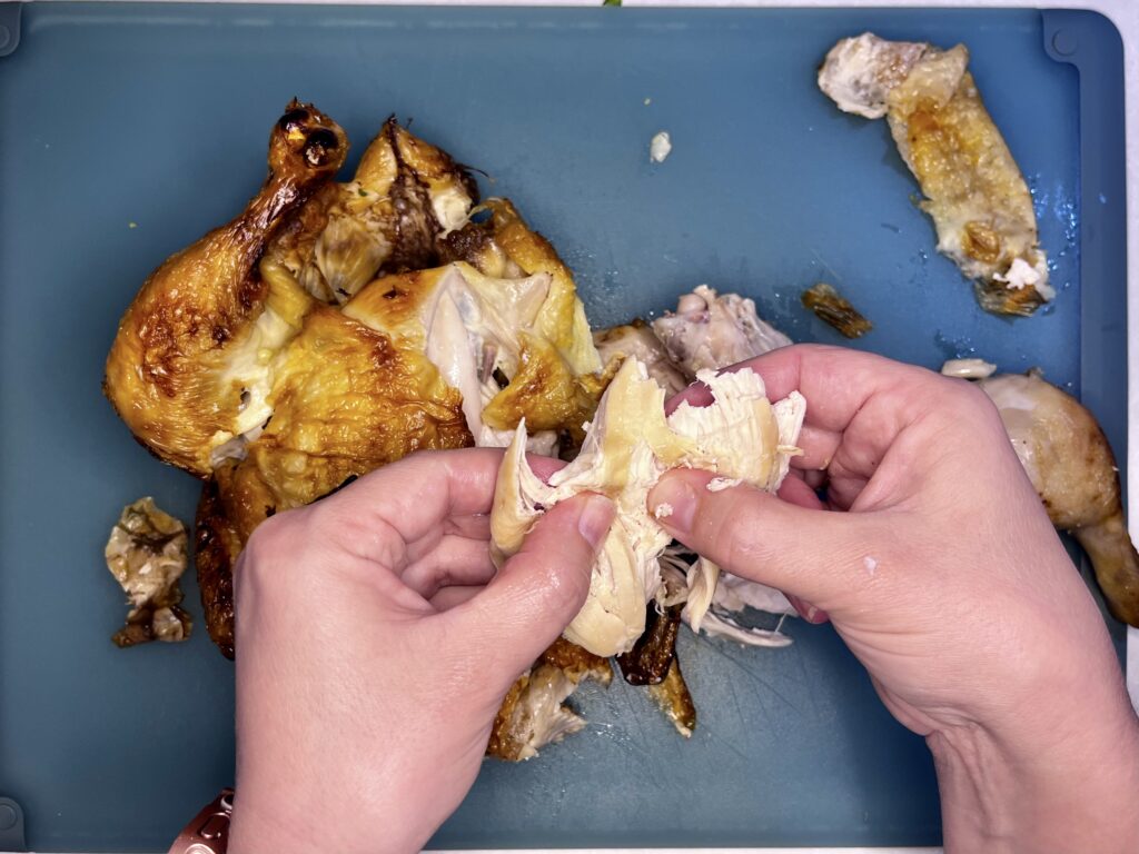 a rotisserie chicken being pulled apart by hand