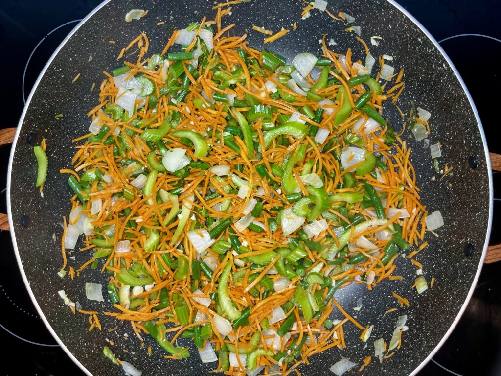 shredded carrots being cooked in a pot with celery, garlic, green beans, and onion