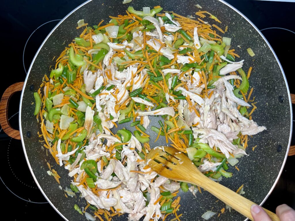 chicken being stirred into vegetable mix