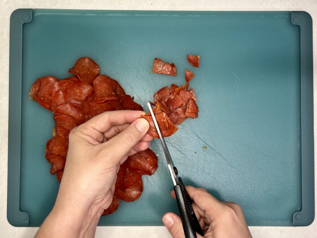 pepperoni being cut into small pieces with meat scissors