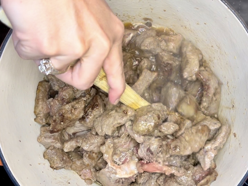 a wooden spoon scraping bottom of pot and stirring beef