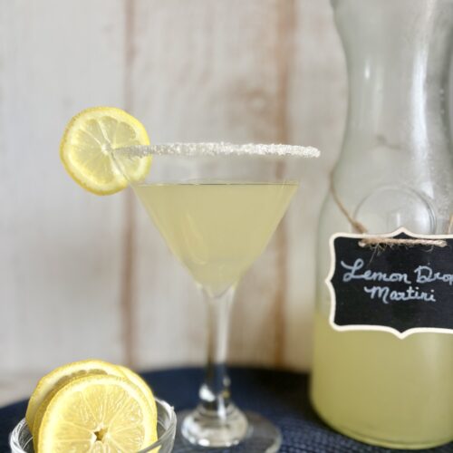 Elegant Lemon Drop Martini garnished with a lemon wheel and sugar-rimmed glass, served alongside a pitcher of fresh lemon cocktail. Perfect for a crowd, this easy pitcher cocktail recipe is ideal for.