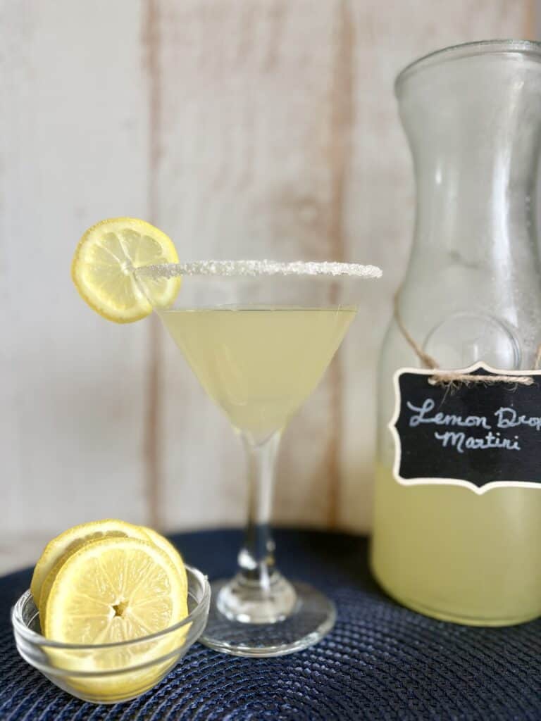 Elegant Lemon Drop Martini garnished with a lemon wheel and sugar-rimmed glass, served alongside a pitcher of fresh lemon cocktail. Perfect for a crowd, this easy pitcher cocktail recipe is ideal for.