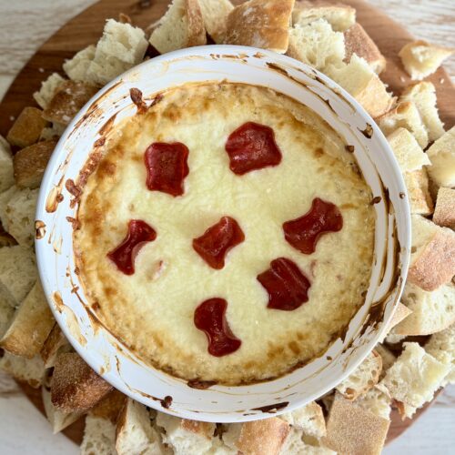 cooked pizza dip in a dish surrounded by bread on a wooden board