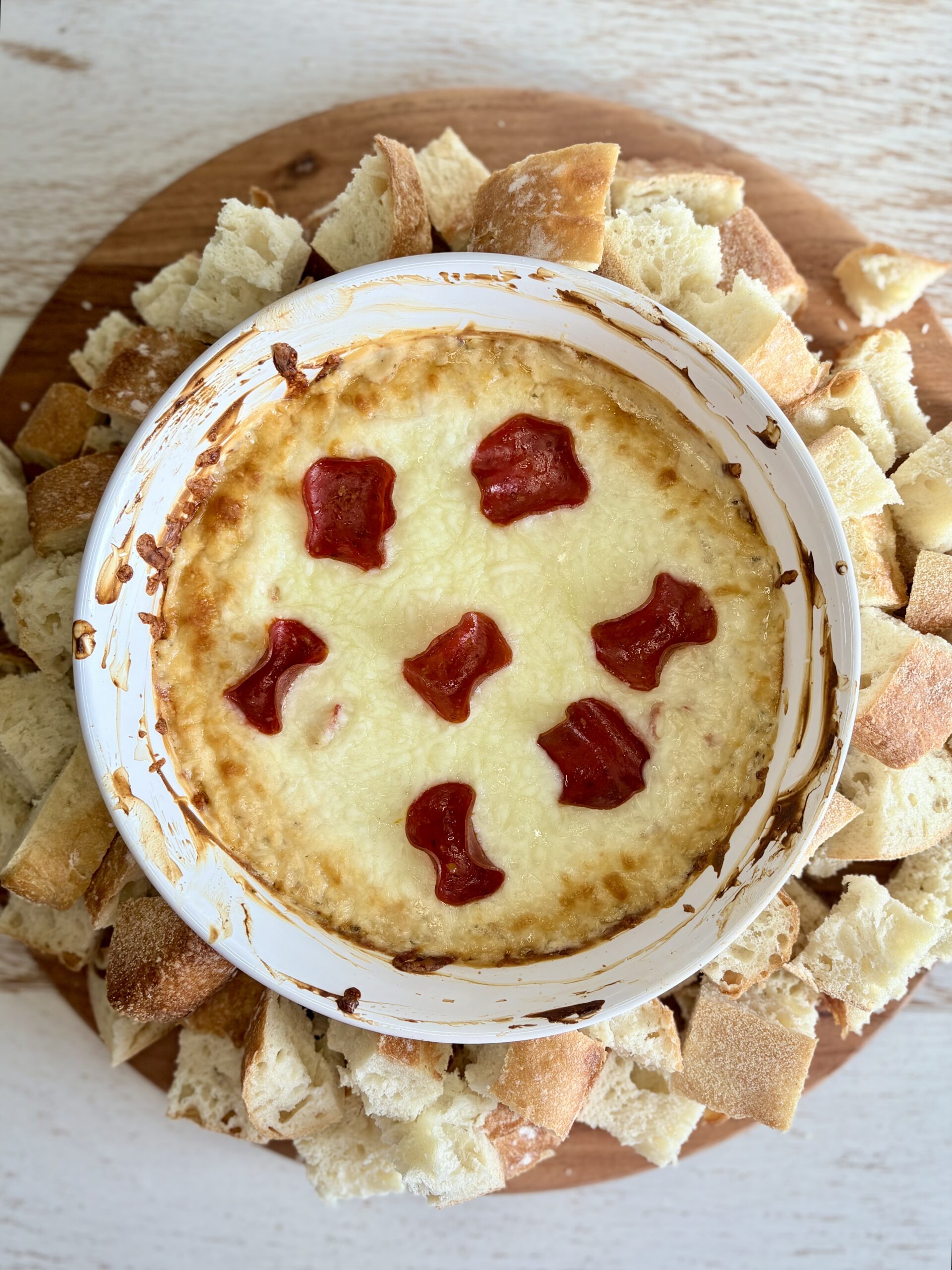 cooked pizza dip in a dish surrounded by bread on a wooden board