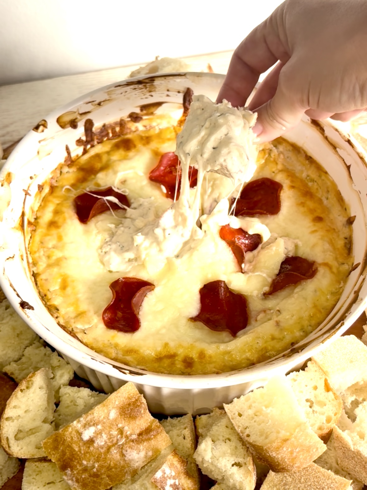 a hand dipping bread into creamy white pizza dip