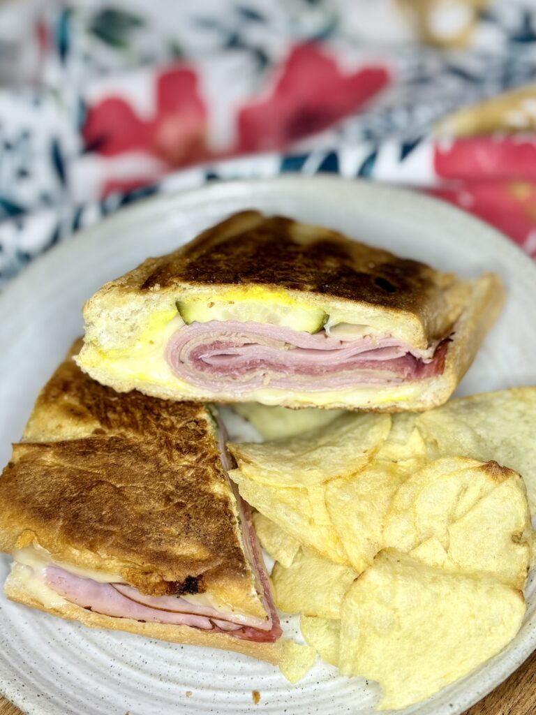 a pressed cuban sandwich on a plate next to potato chips