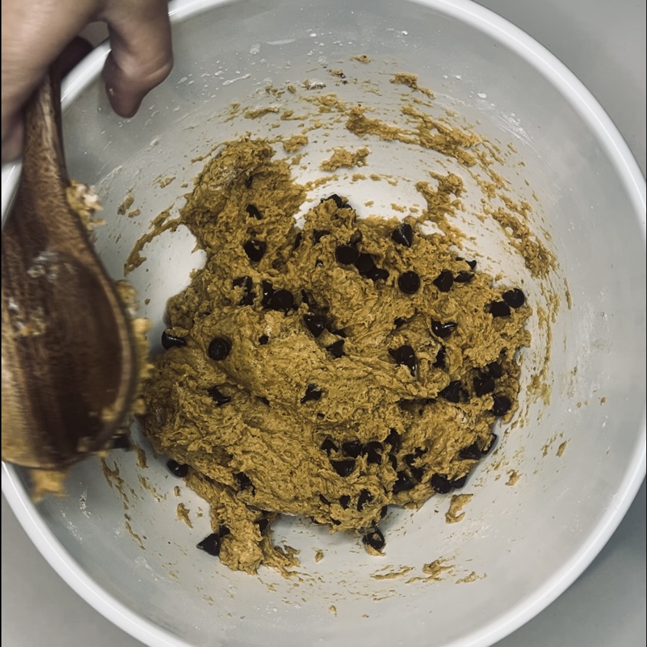 Flour, pumpkin pie spice, baking powder, baking soda, salt and chocolate chips being mixed with a wooden spoon in a large bowl
