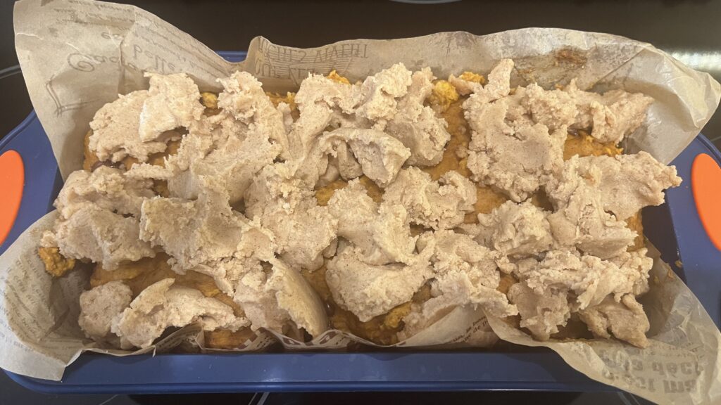 Cake batter topped with streusel topping in a parchment paper lined loaf pan.
