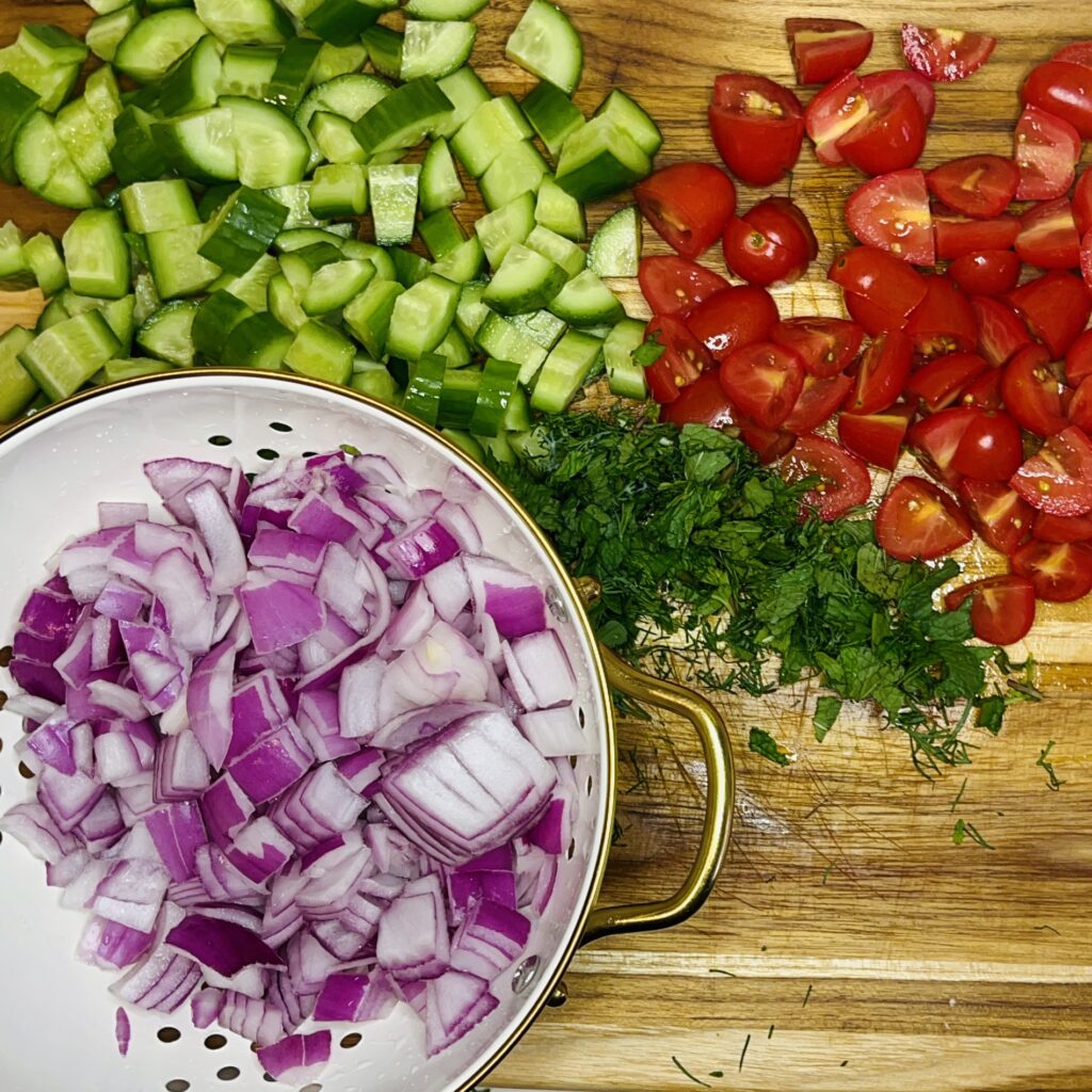 Drained onions, diced cucumbers, quartered tomatoes on a cutting board.
