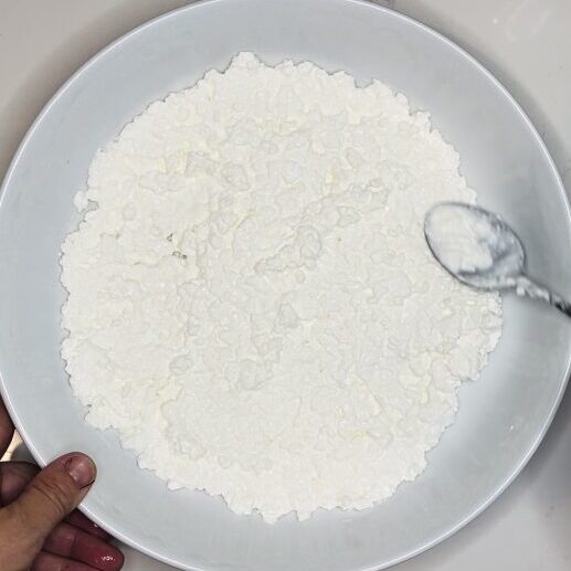 Cottage cheese being spread onto the base of a low rimmed bowl.
