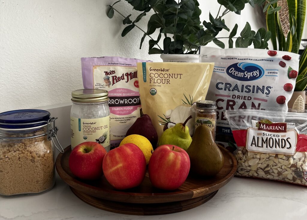 Ingredients for gluten free crumble and filling, Dried cranberries, 3 apples, 3 pears, sliced almonds, cinnamon, arrowroot, coconut flour, coconut oil, brown sugar on the. counter
