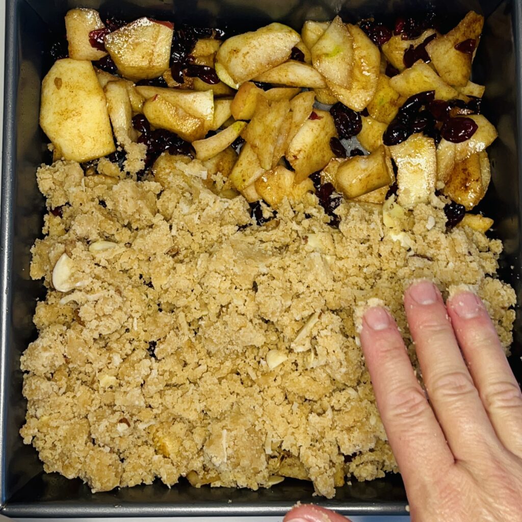 gluten free crumble being applied to a fruit filling in a baking dish.