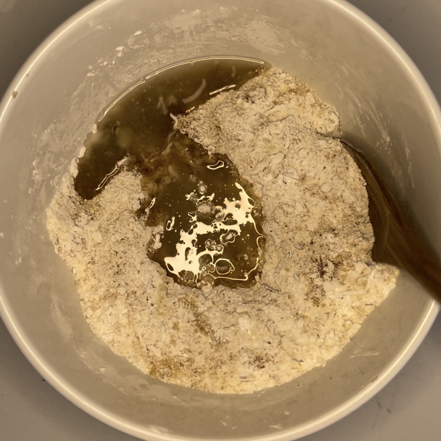 coconut flour, arrowroot flour, almonds, shredded coconut, cinnamon, sugar and coconut oil in a bowl getting mixed together.
