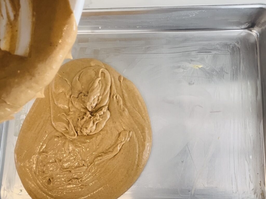 Pouring prepared batter onto a greased 18x13 inch rimmed baking sheet.
