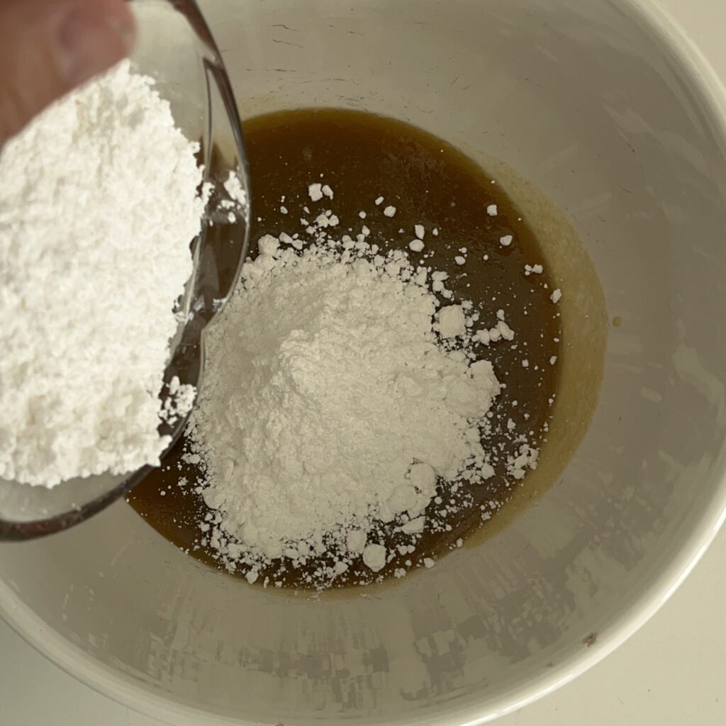 Adding confectioners' sugar to the cooled butter, brown sugar and milk also added to a large mixing bowl
