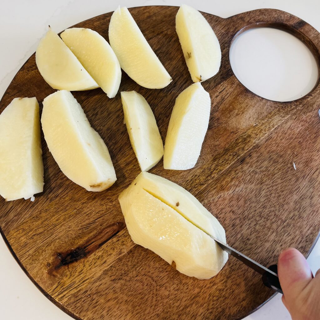 Cutting peeled potatoes into quarters lengthwise on a cutting board
