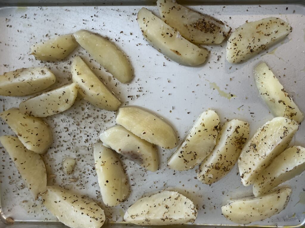 Potatoes on a lined baking sheet with oregano, lemon juice and water.
