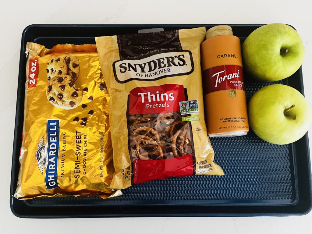 Green apples, pretzels, 24 oz semi-sweet chocolate chips and caramel sauce on a baking sheet