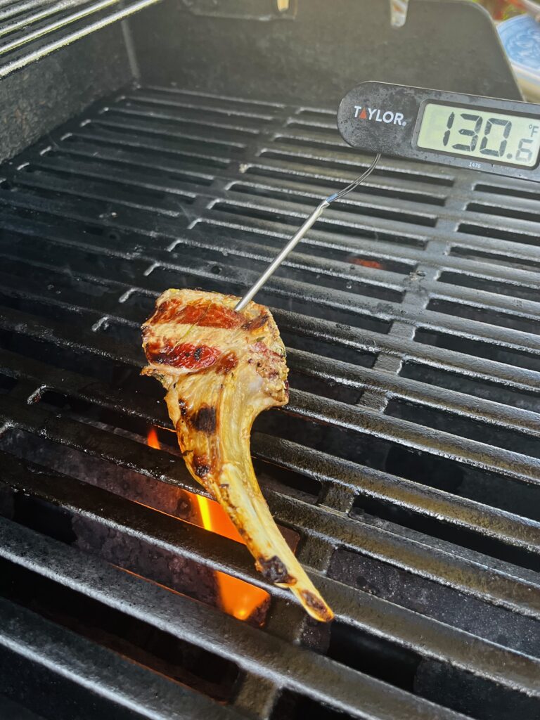 An inserted meat thermometer into a lamb chop on the grill