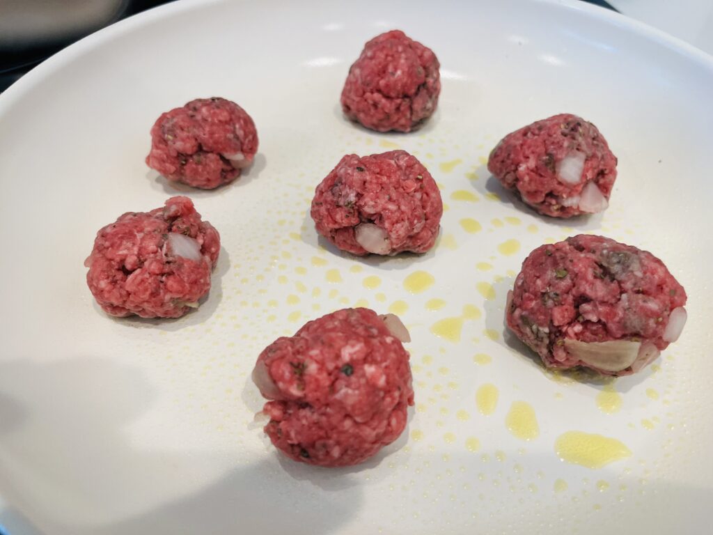 Uncooked meatballs in a non-stick frying pan.