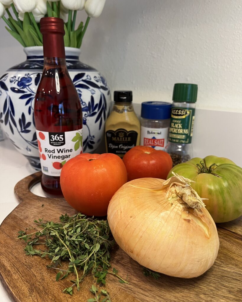 Red wine vinegar, heirloom tomatoes, vadalia onion, fresh thyme, salt and pepper, dijon mustard on a cutting board