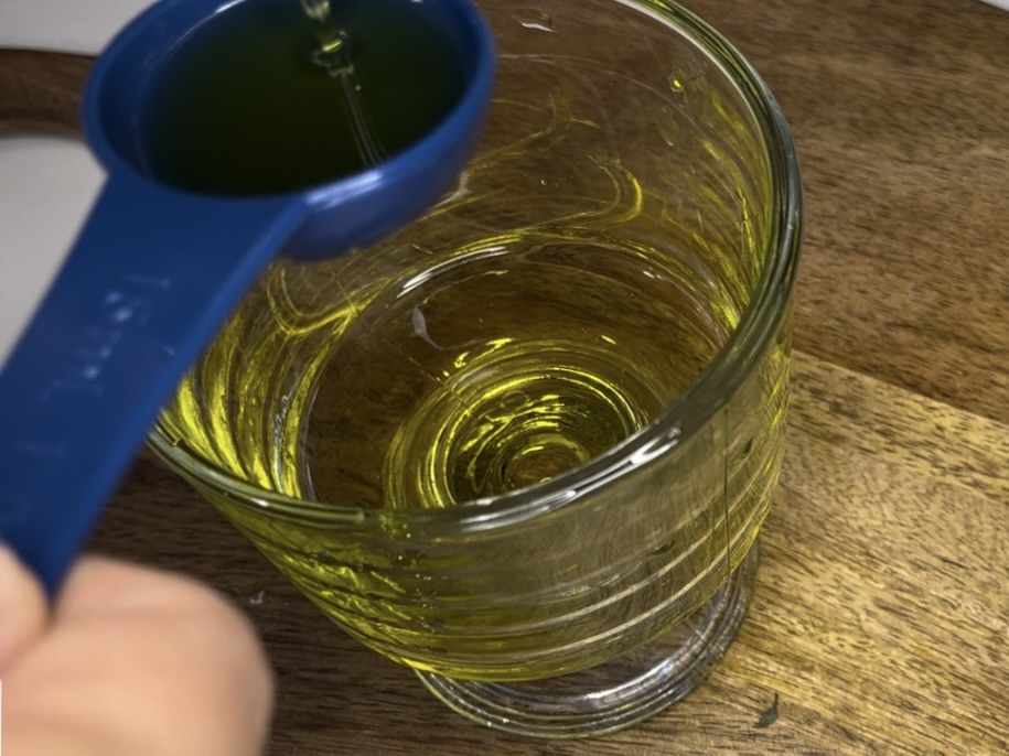 Adding olive oil with a measuring spoon into a glass bowl